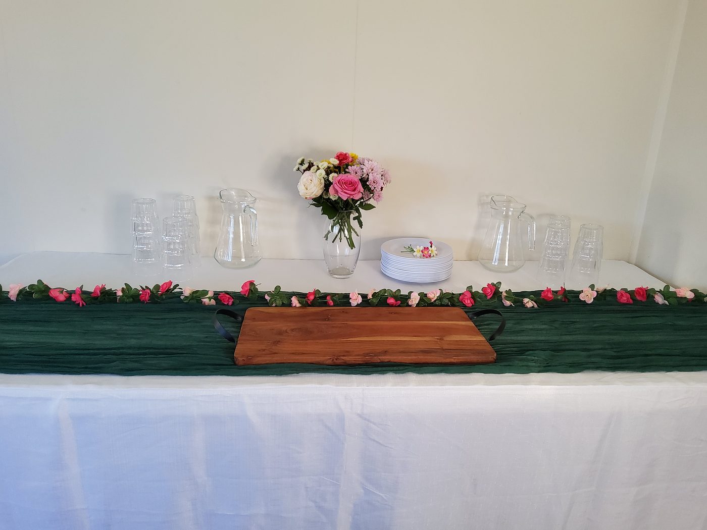 Party table with green cheesecloth runner and pink rose garland on white cloth